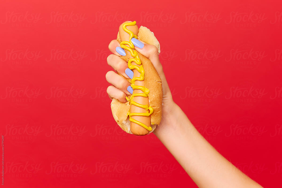Woman\'s hand with blue painted nails holds hotdog tightly