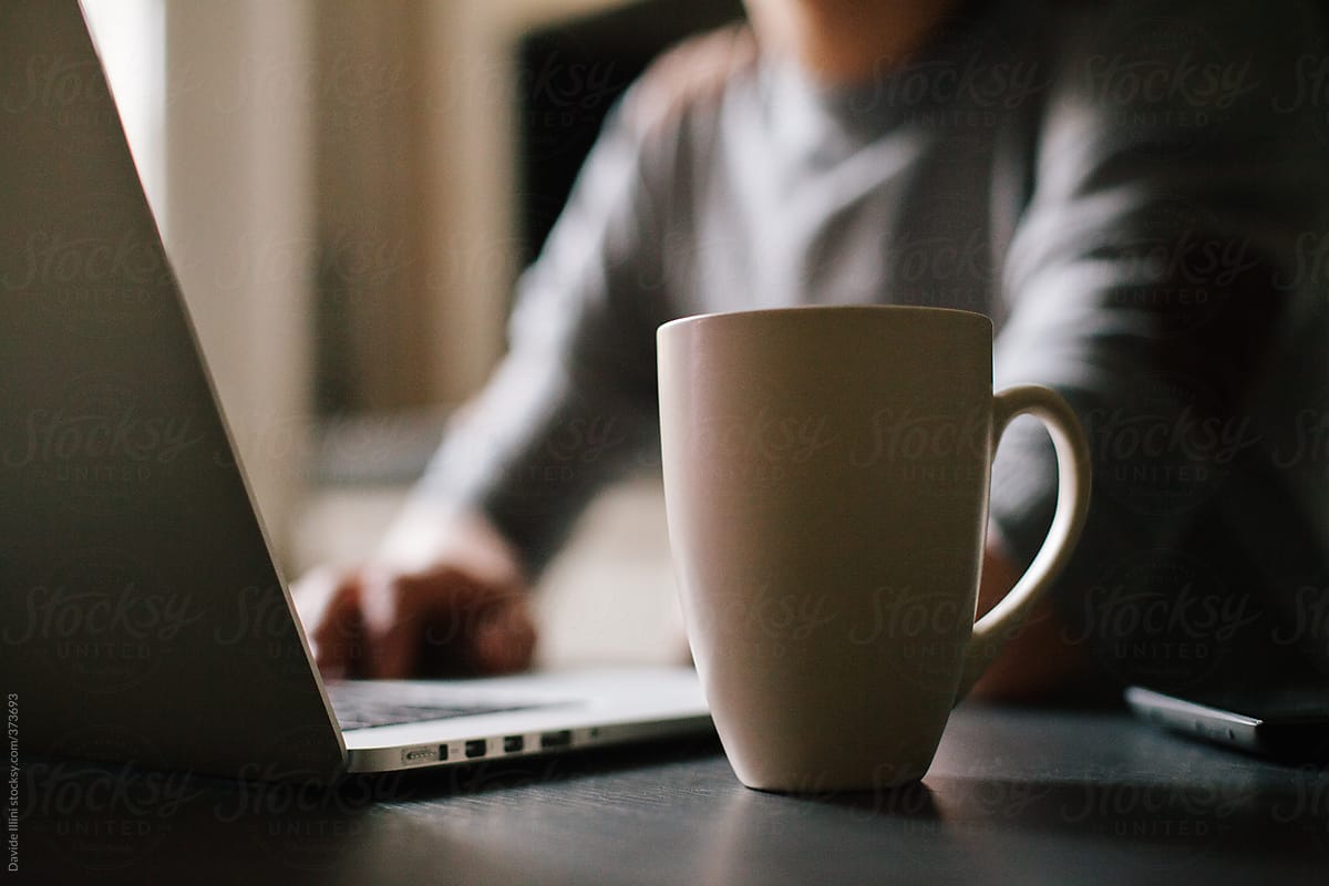 Cup of coffee on the table. Young man blurred using the laptop.