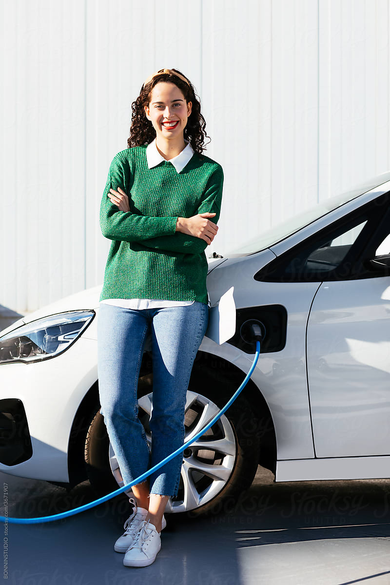 Happy woman leaning on charging electric vehicle