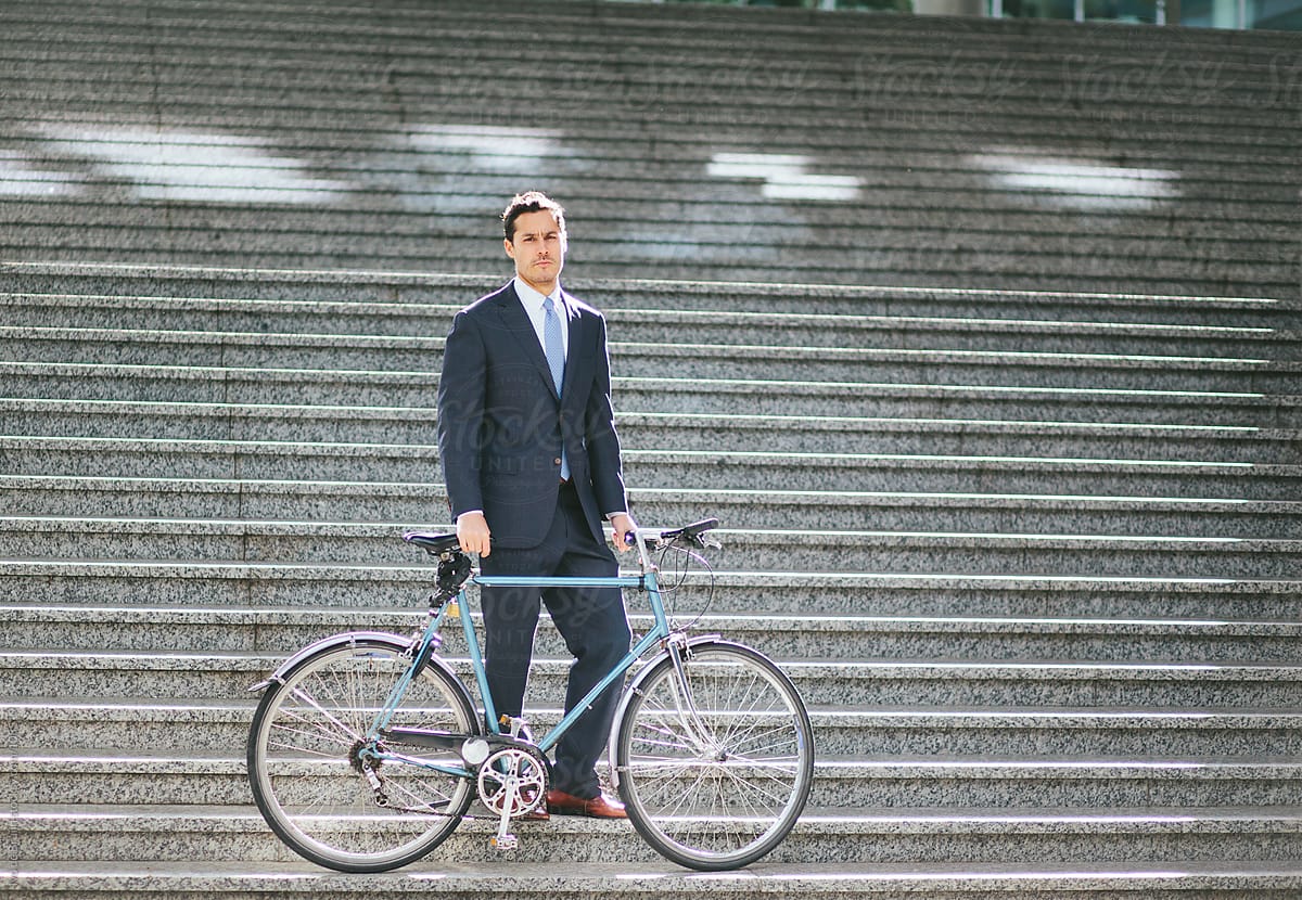 Serious young business man in suit standing with his bike on a s