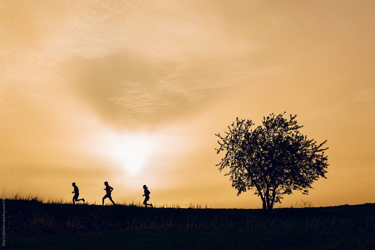 group of men running trail outside in nature with trees at sunrise.