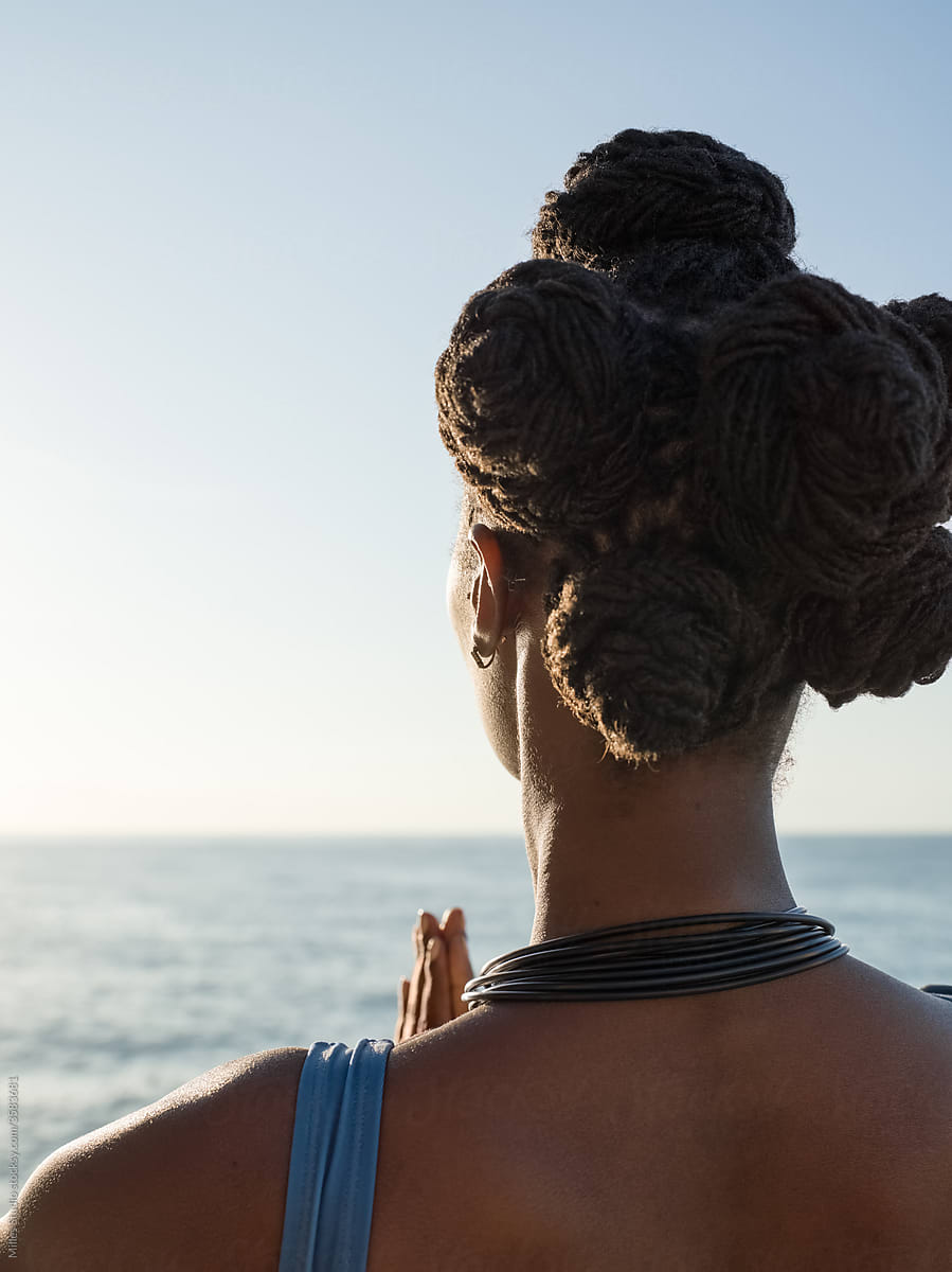 Black female meditating at sunrise near sea