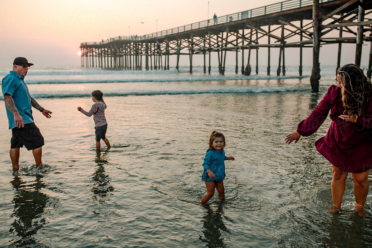 Family wading in ocean near pier at sunset