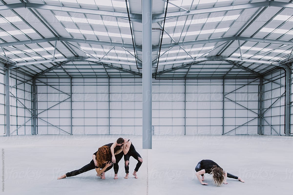 Three dancers moving together, and a solo dancer, in an empty warehouse