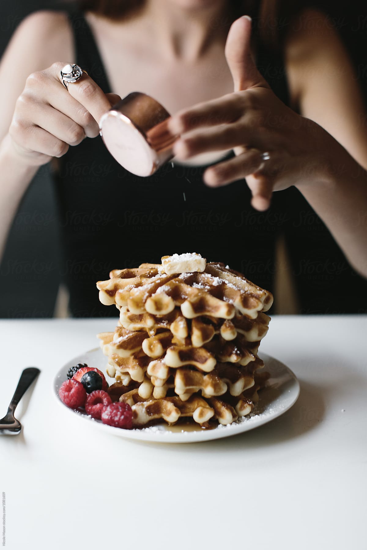 person putting powdered sugar on stack of waffles