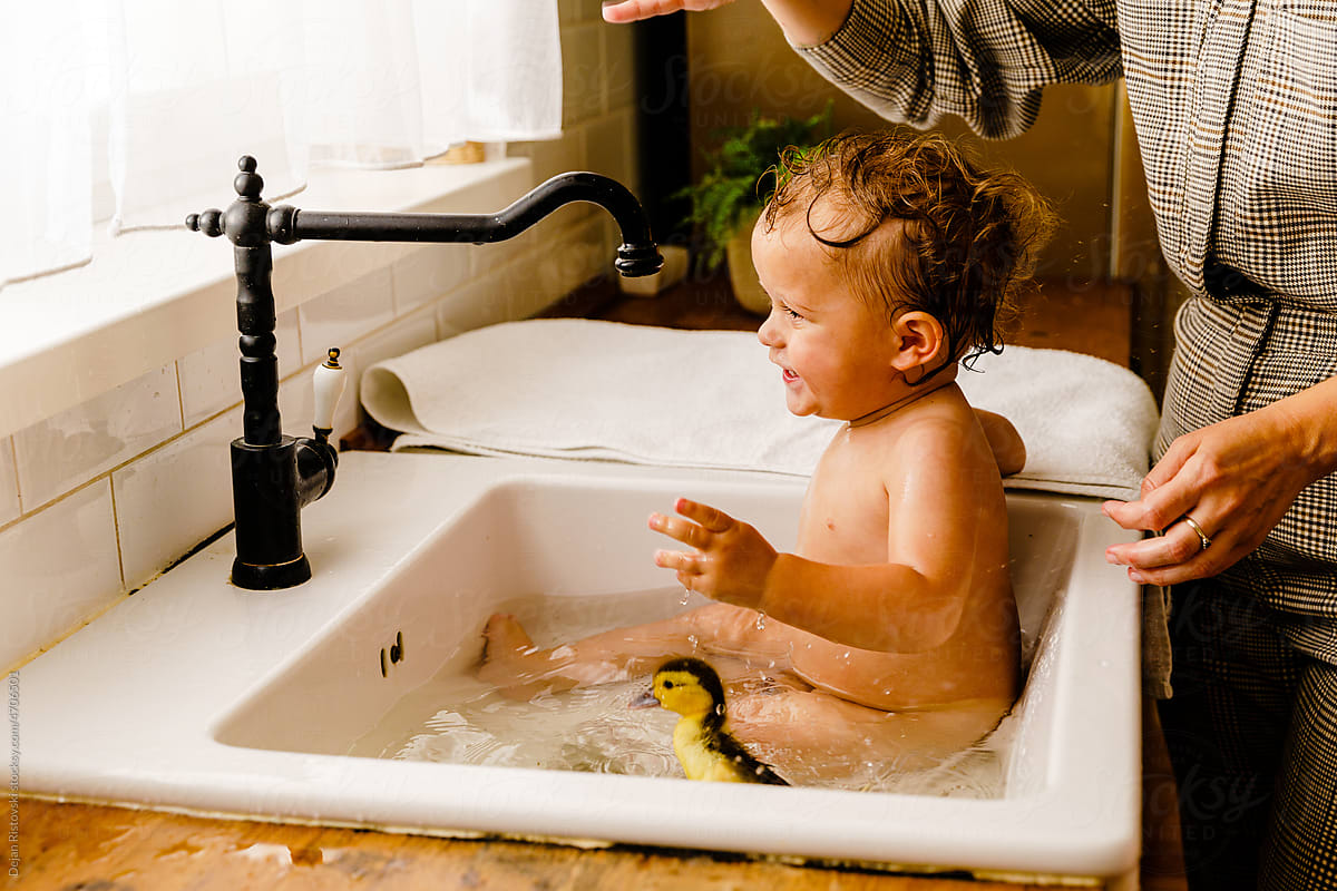Baby playing with ducks in the kitchen sink