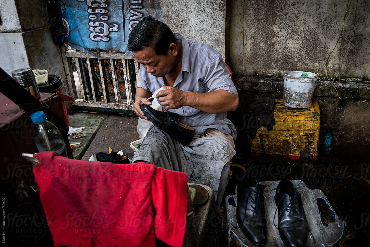 A shoemaker glues the sole of a shoe on the street in Cambodia