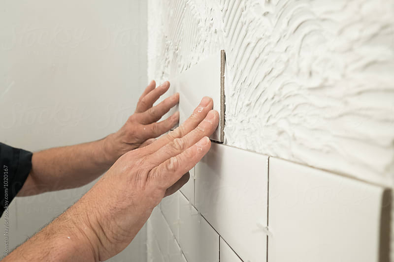Man laying white tiles in bathroom shower