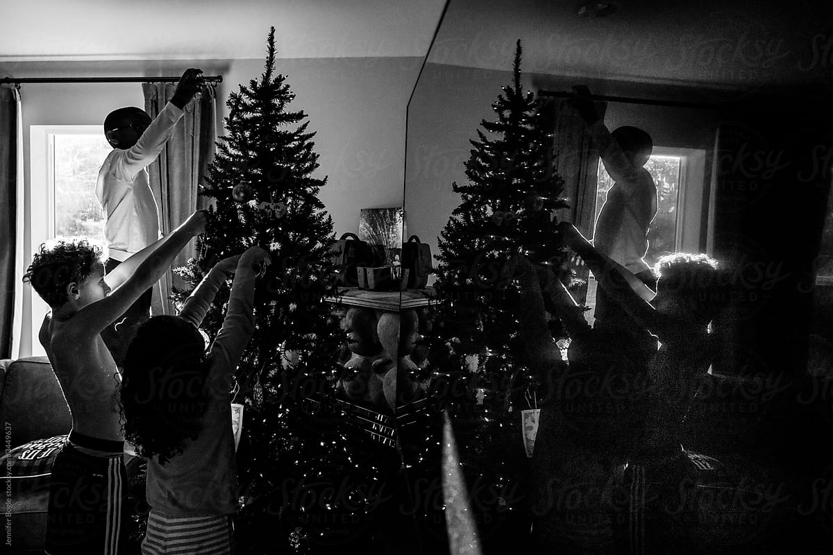 black and white low light siblings decorate Christmas tree