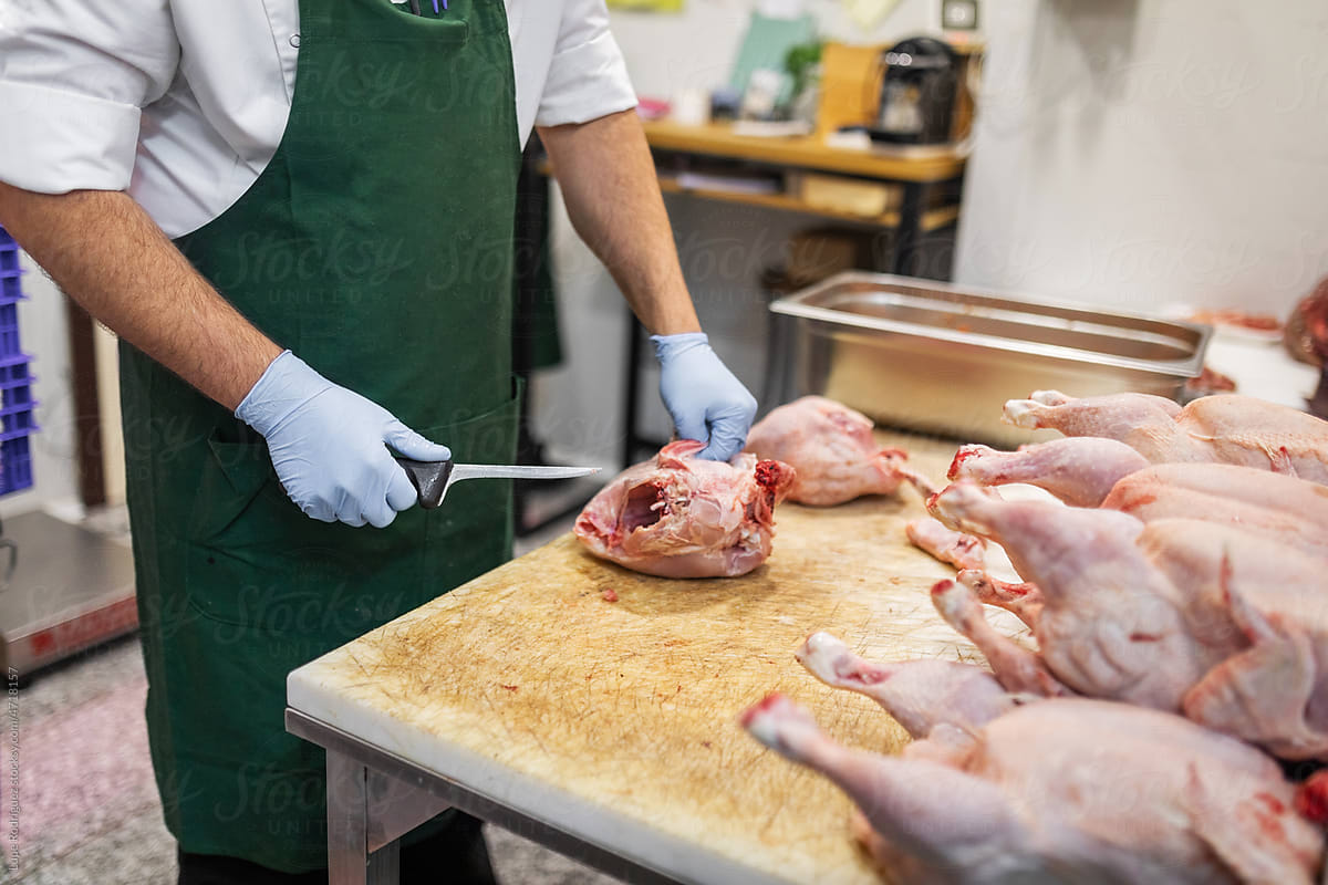 anonymous man cutting chicken meat in the back of a butcher shop