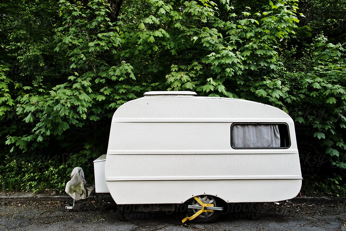 Parked oldfashioned Camper-trailer before green trees