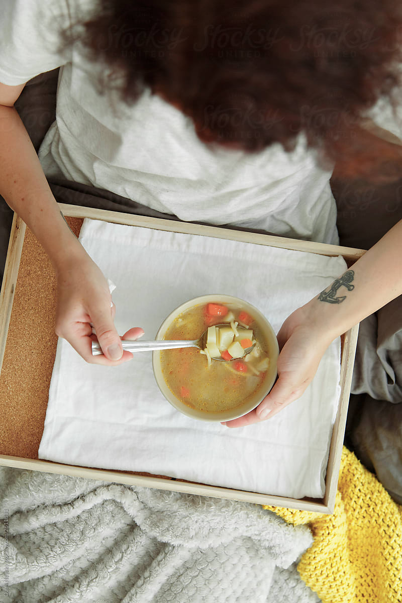 Unrecognizable ill female eating broth in bed
