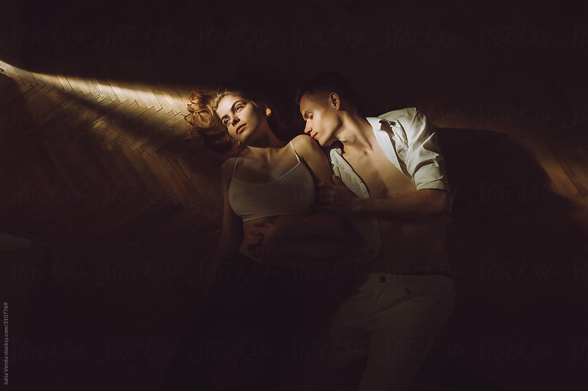 A young man and woman lie on the sun ray oin the dark room