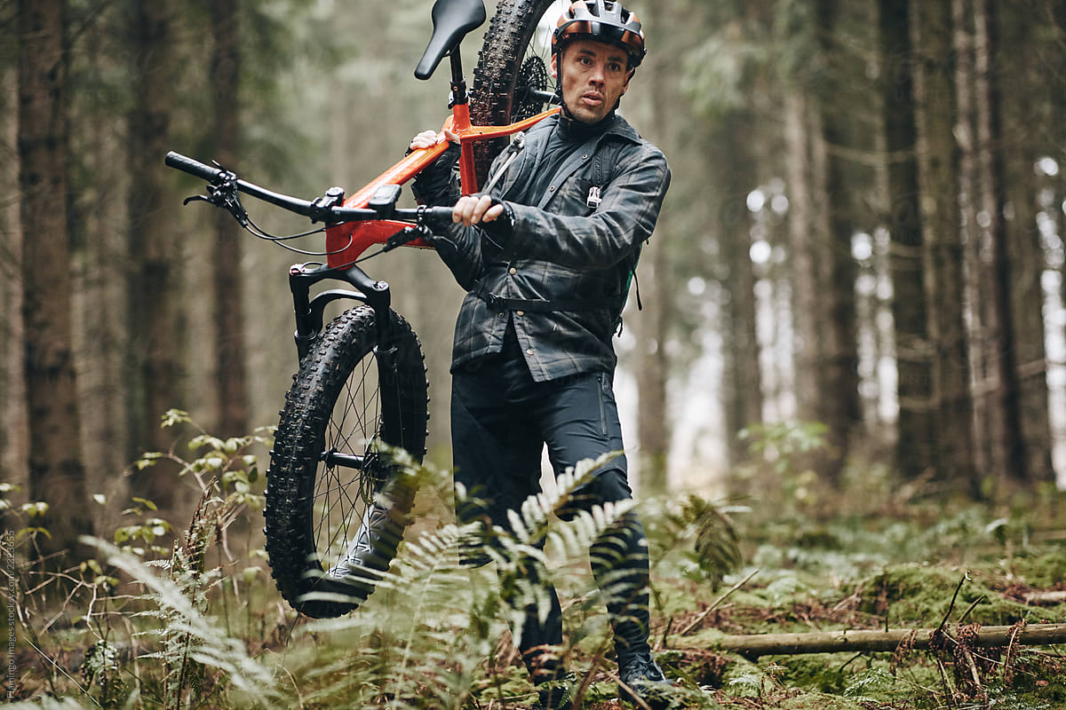 Rider carrying his mountain bike along a dense forest trail