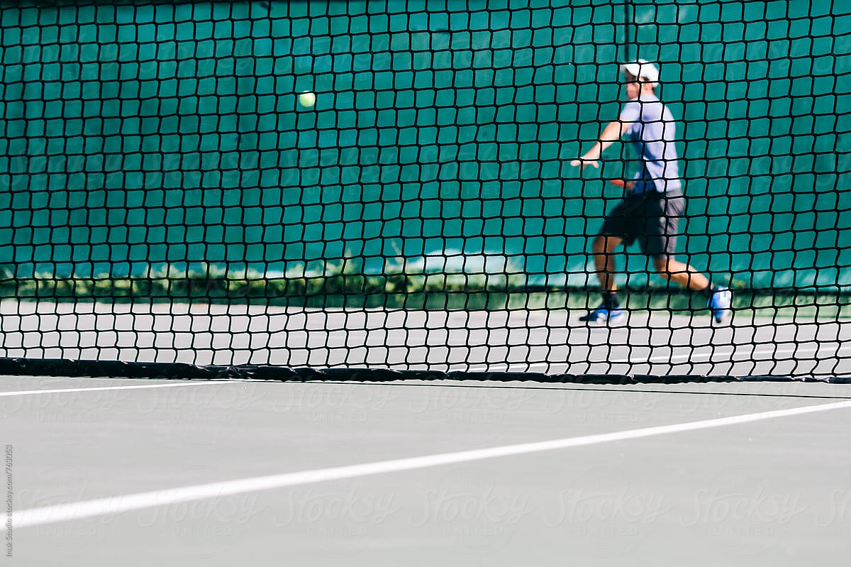 Tennis player seen behind the net in a tennis court playing a match