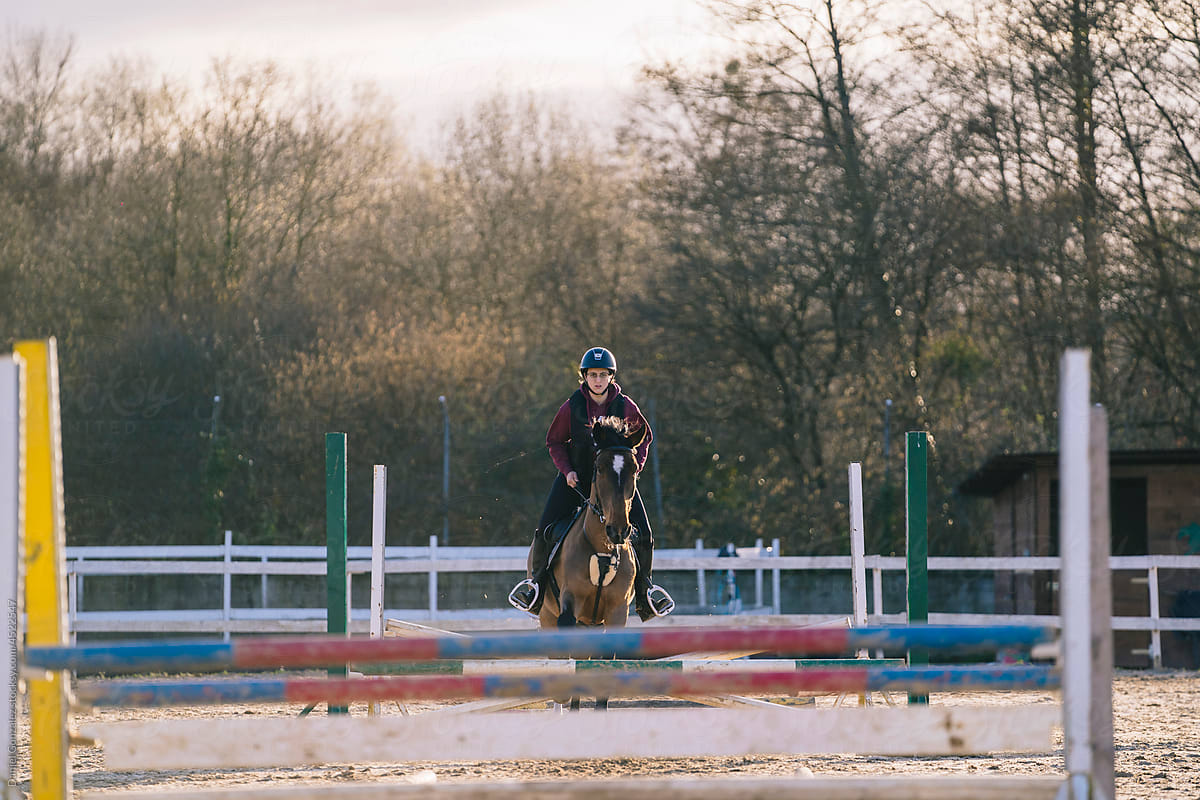 Serious female equestrian riding horse over barriers