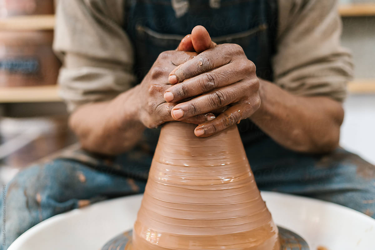 Crop black potter shaping clay vase on wheel
