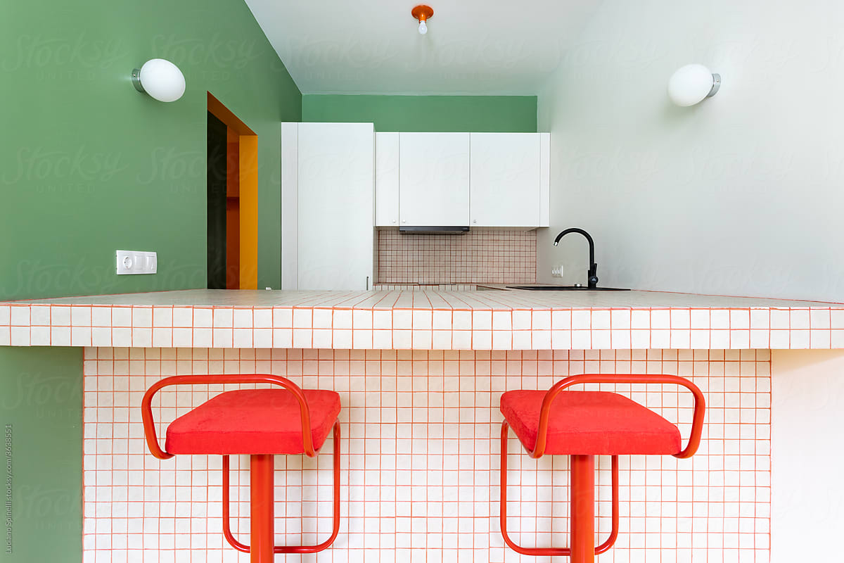 Two red stools in a colourful kitchen with symmetric round lamps