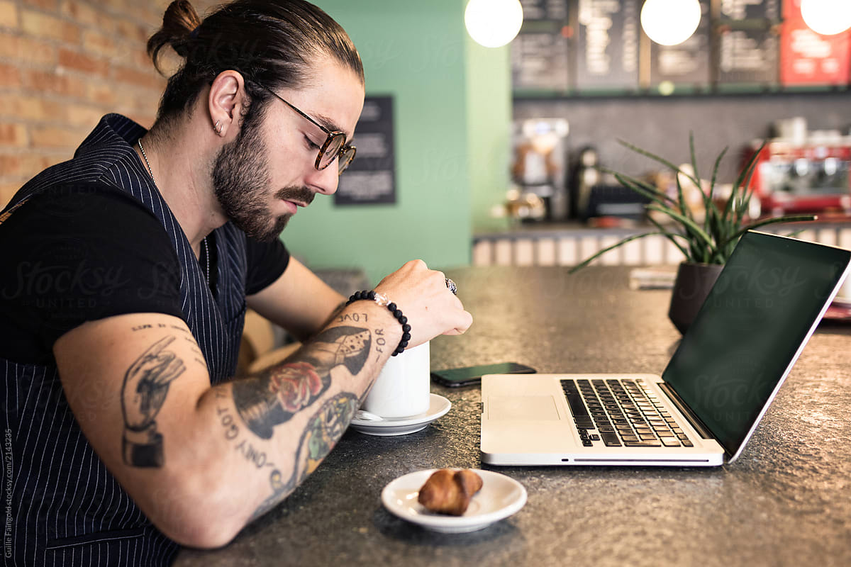 Trendy tattooed man in a coffee shop with laptop.