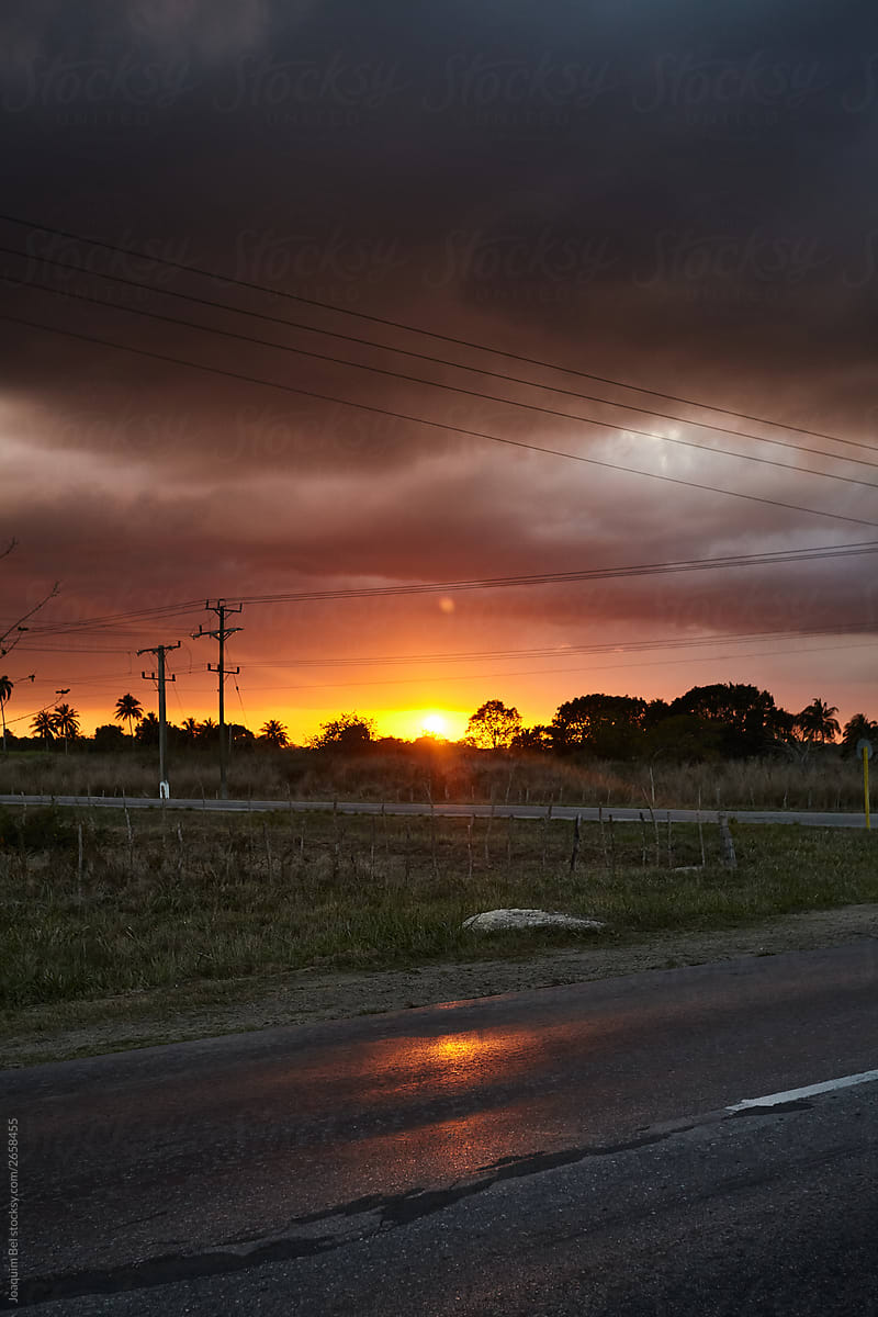 Sun setting over road and field in gloomy sky