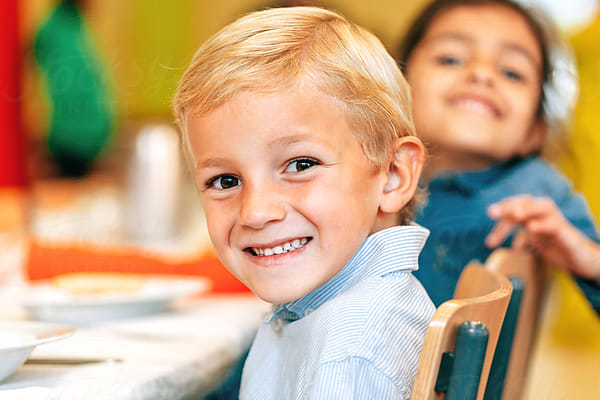 Two Funny Kids Looking At Camera While Eating In School Canteen by Stocksy  Contributor VICTOR TORRES - Stocksy