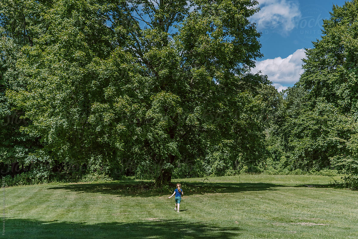 A little girl runs toward a big green tree.