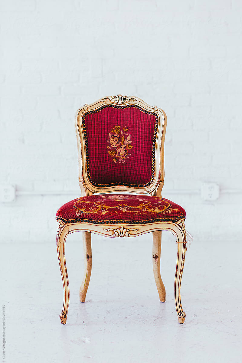 Vintage red embroidered chair seat with golden legs in a white studio