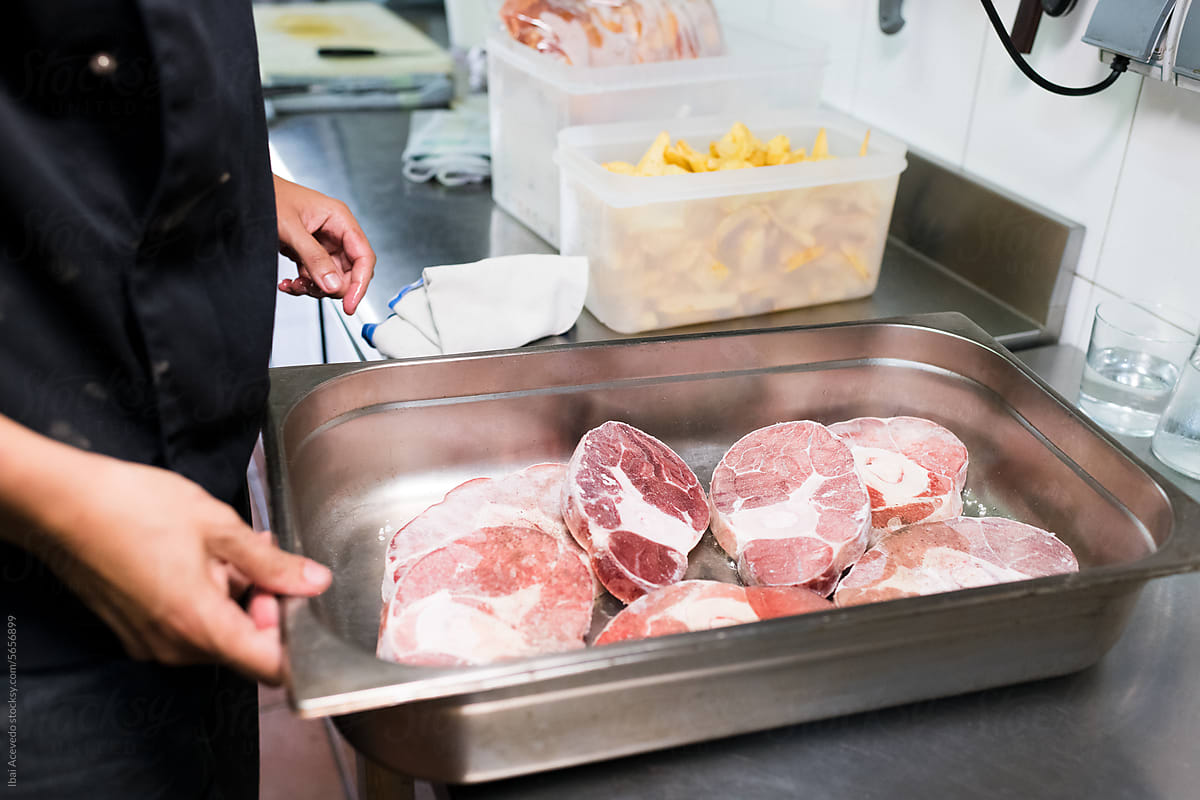 Chef holding metal tray with frozen meat
