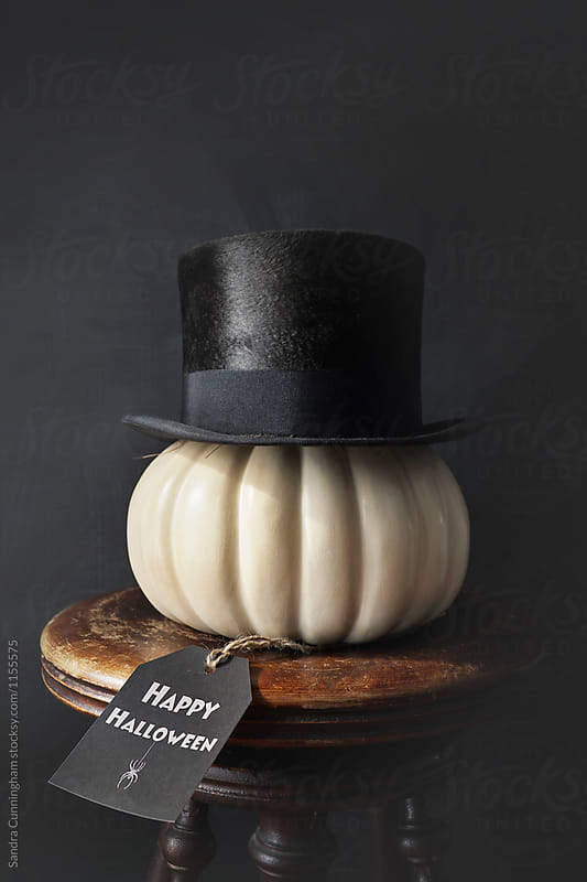 Closeup of white painted pumpkin with top hat on bench