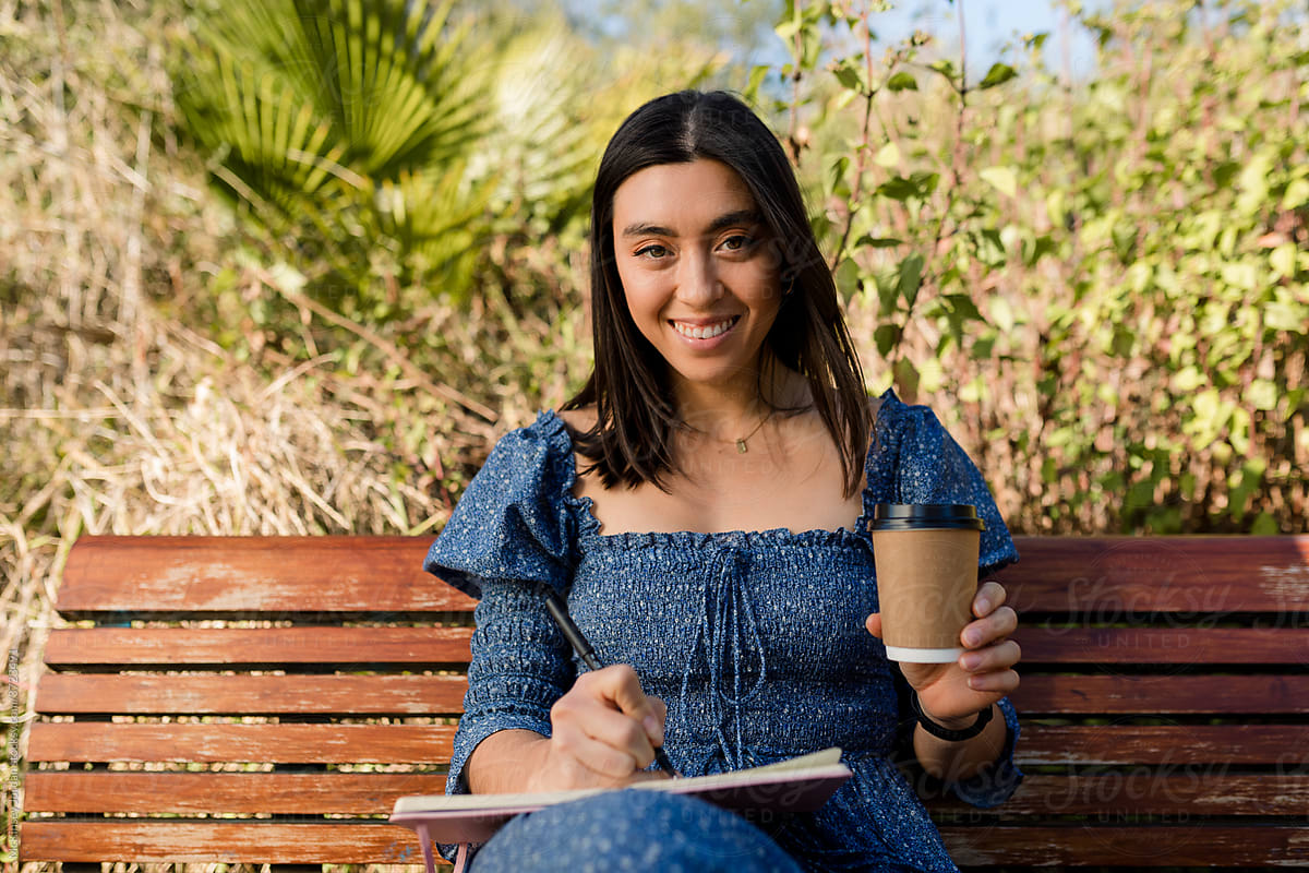 Young Woman Sitting on a Bench Writes While Drinking Coffee