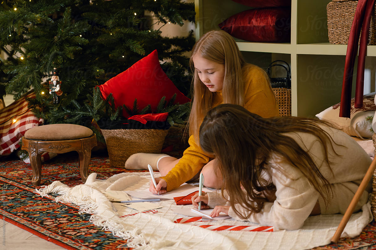 Sisters writing letters to Santa near Christmas tree