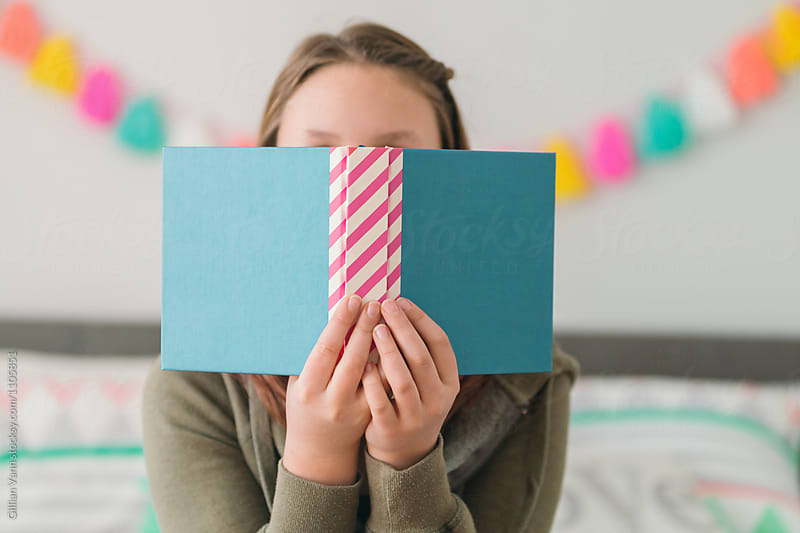 teen girl hiding behind a book with blank cover, blues and pinks