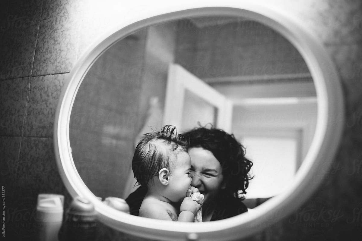 Mother and baby laughing seen in bathroom mirror.