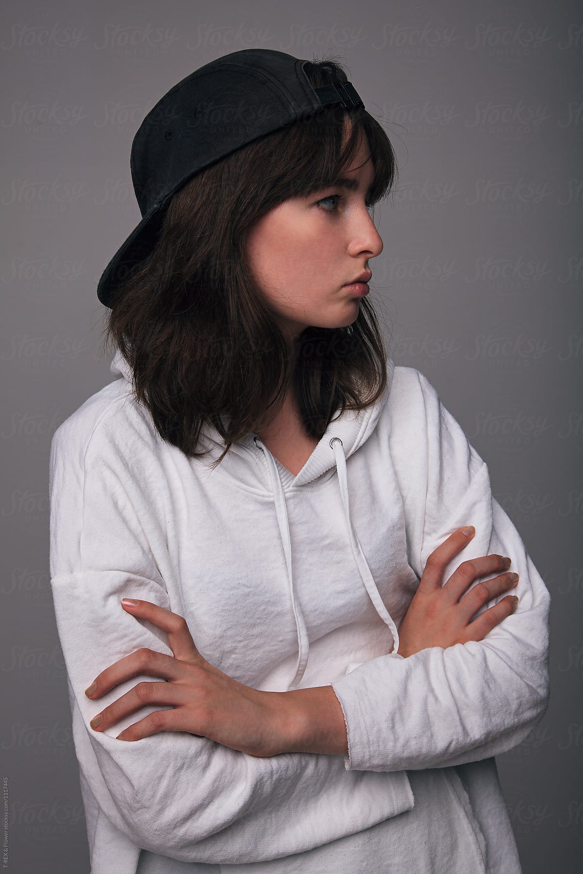Teen Girl In Cap With Arms Folded Looking Away With Indifference By