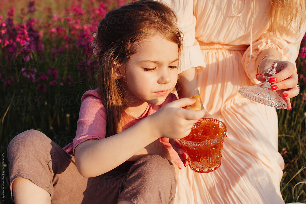 Girl eating jam during picnic with mother