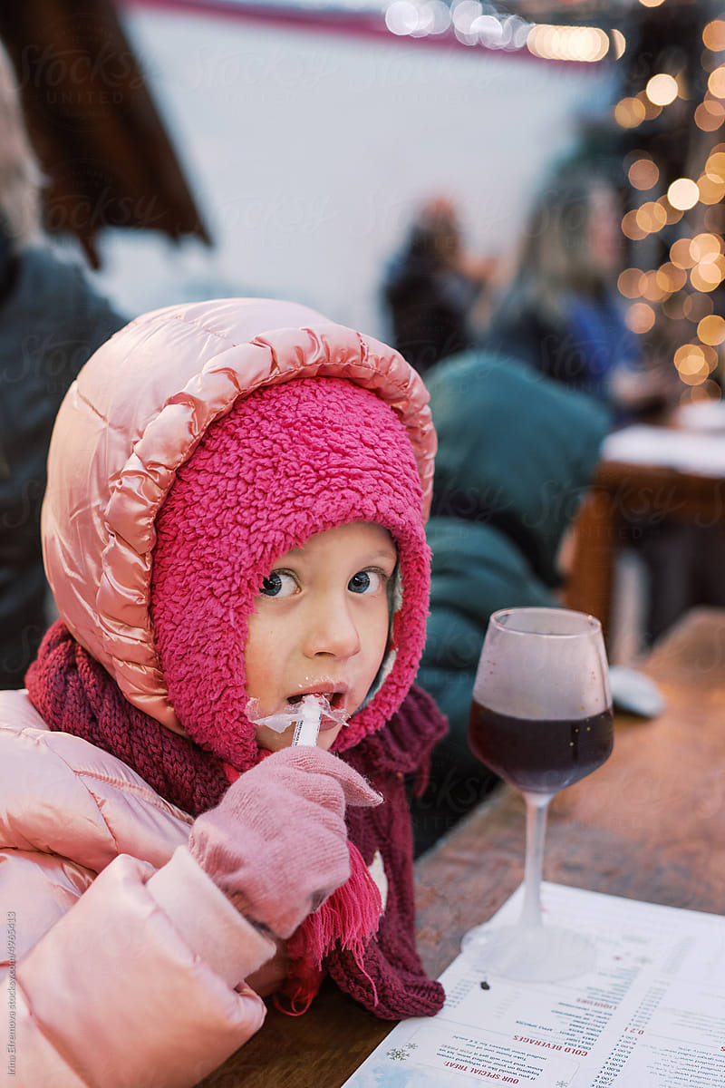 Girl in pink winter clothes eats a candy cane
