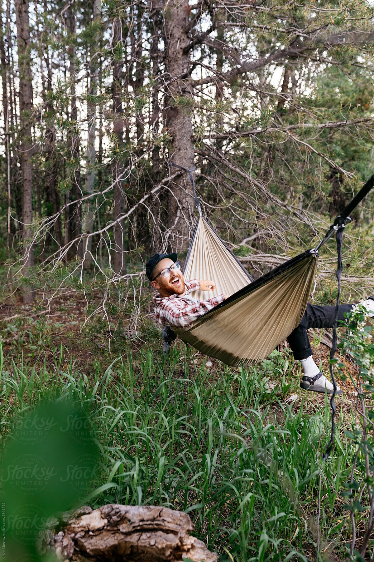 Young male wearing flannel relaxing in hammock while camping in the woods