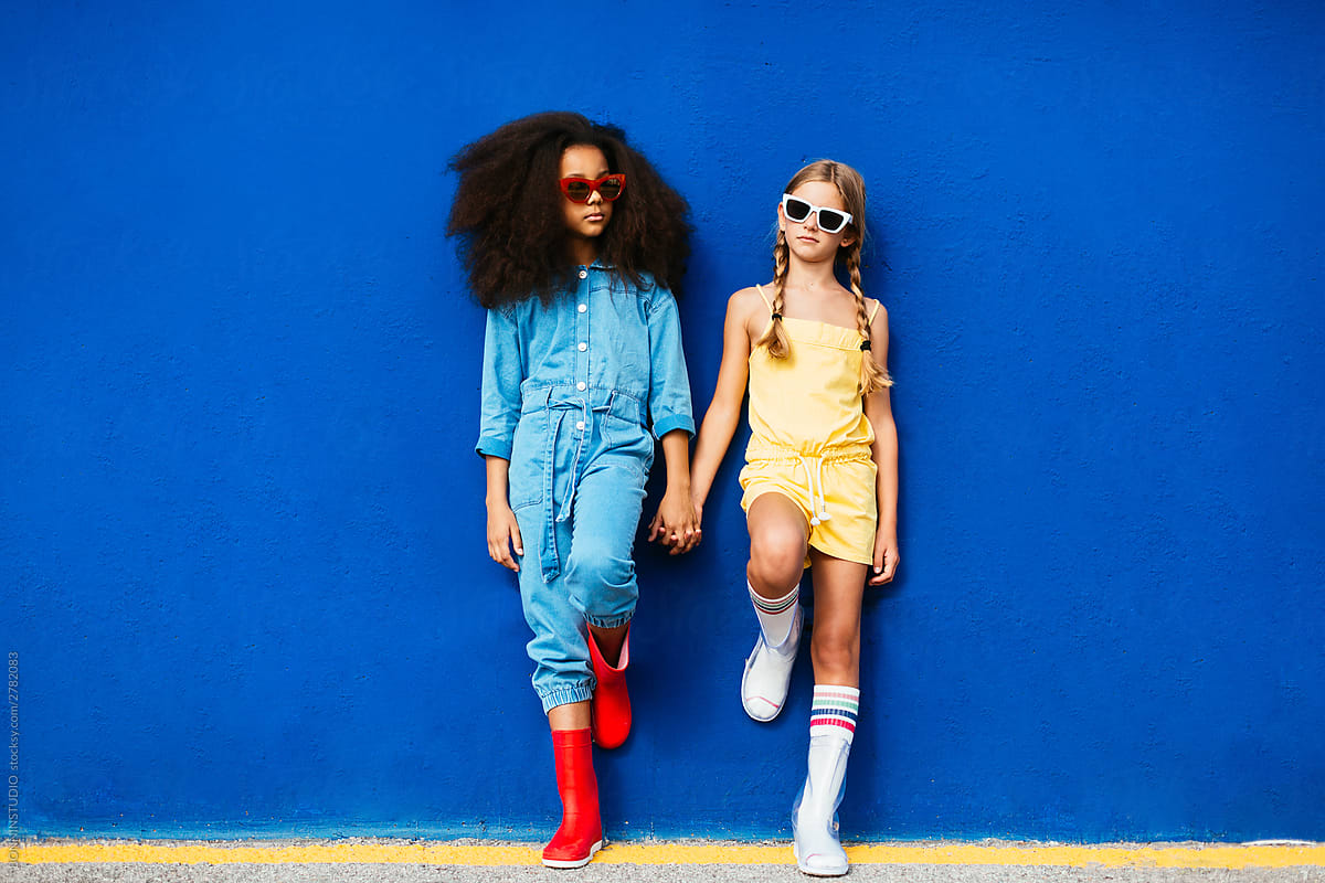 Stylish multiethnic friends in sunglasses holding hands while standing on street