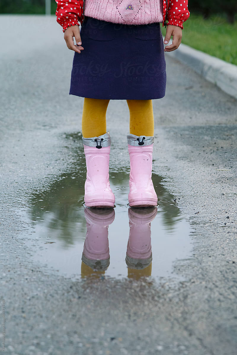 Crop child standing in puddle on road after rain