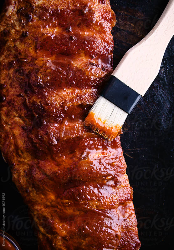 Brushing sauce onto a rack of ribs.
