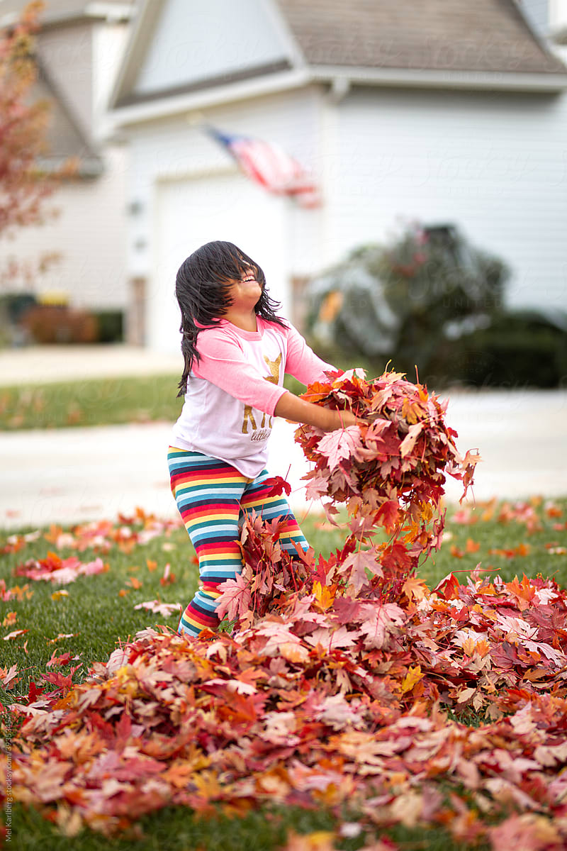 Young girl playing in leaf pile in a neighborhood yard