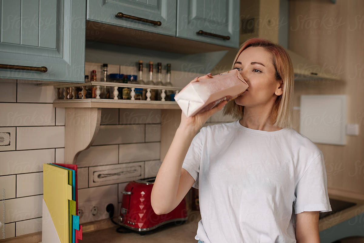 A Girl In A White T-shirt And Pink Hair Is Drinking Milk From The Box At  The Kitchen