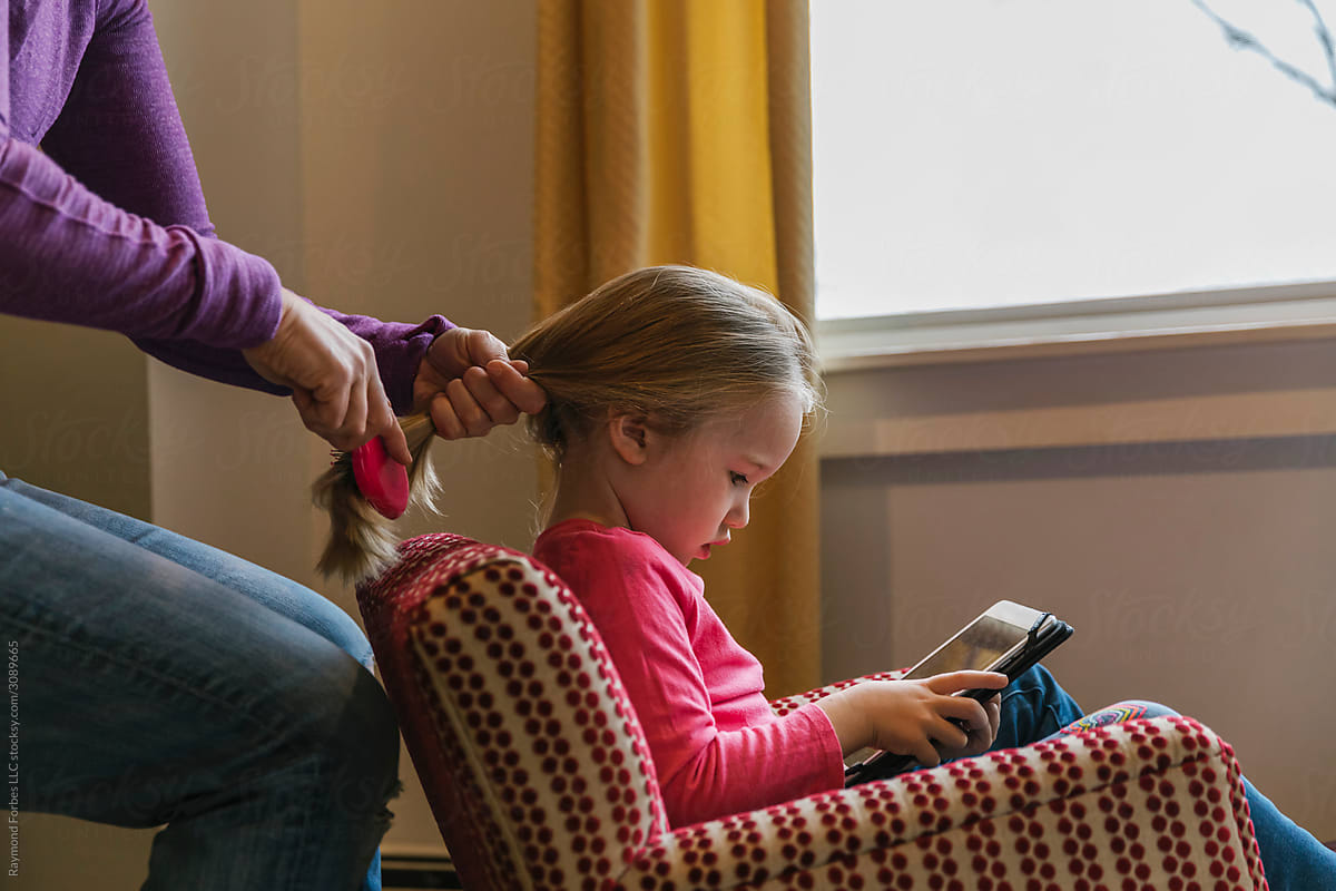 Mother Braiding Young Girls Hair  watching computer