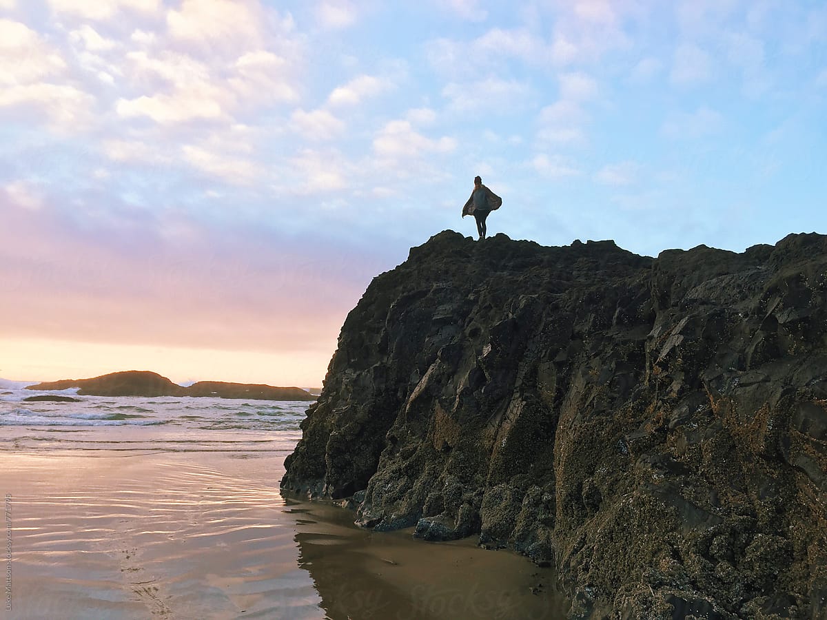 Young Woman Spreading Arms Like Wings On Top Of Rocky Outcrop Along Ocean Shore