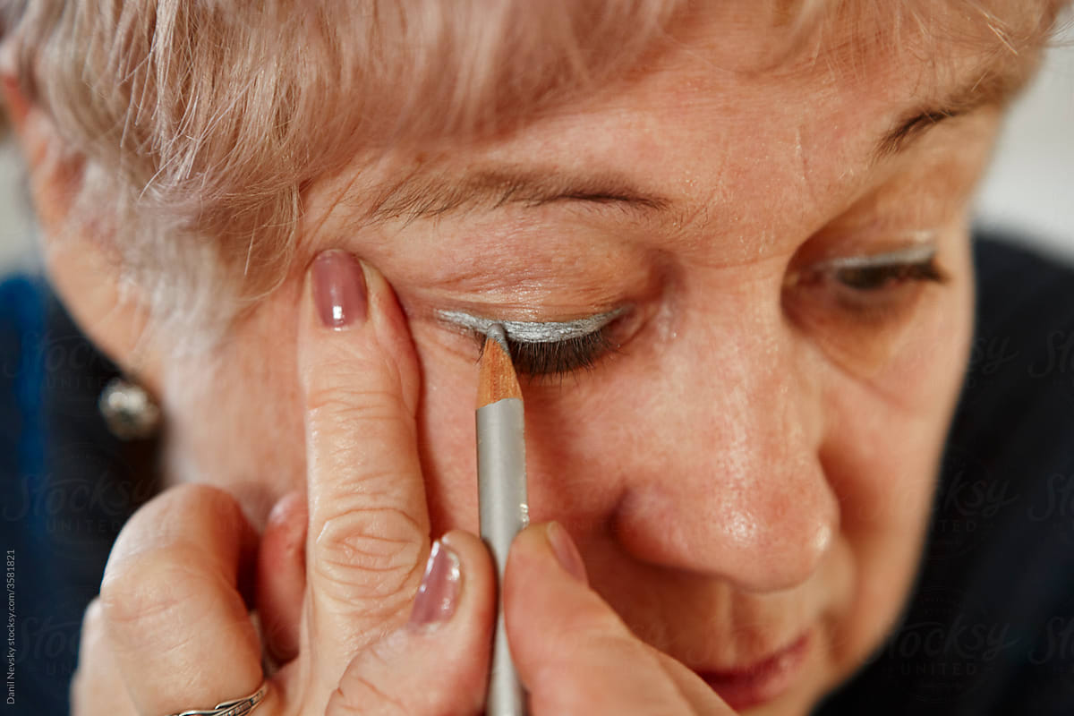Elderly female applying silver eyeliner