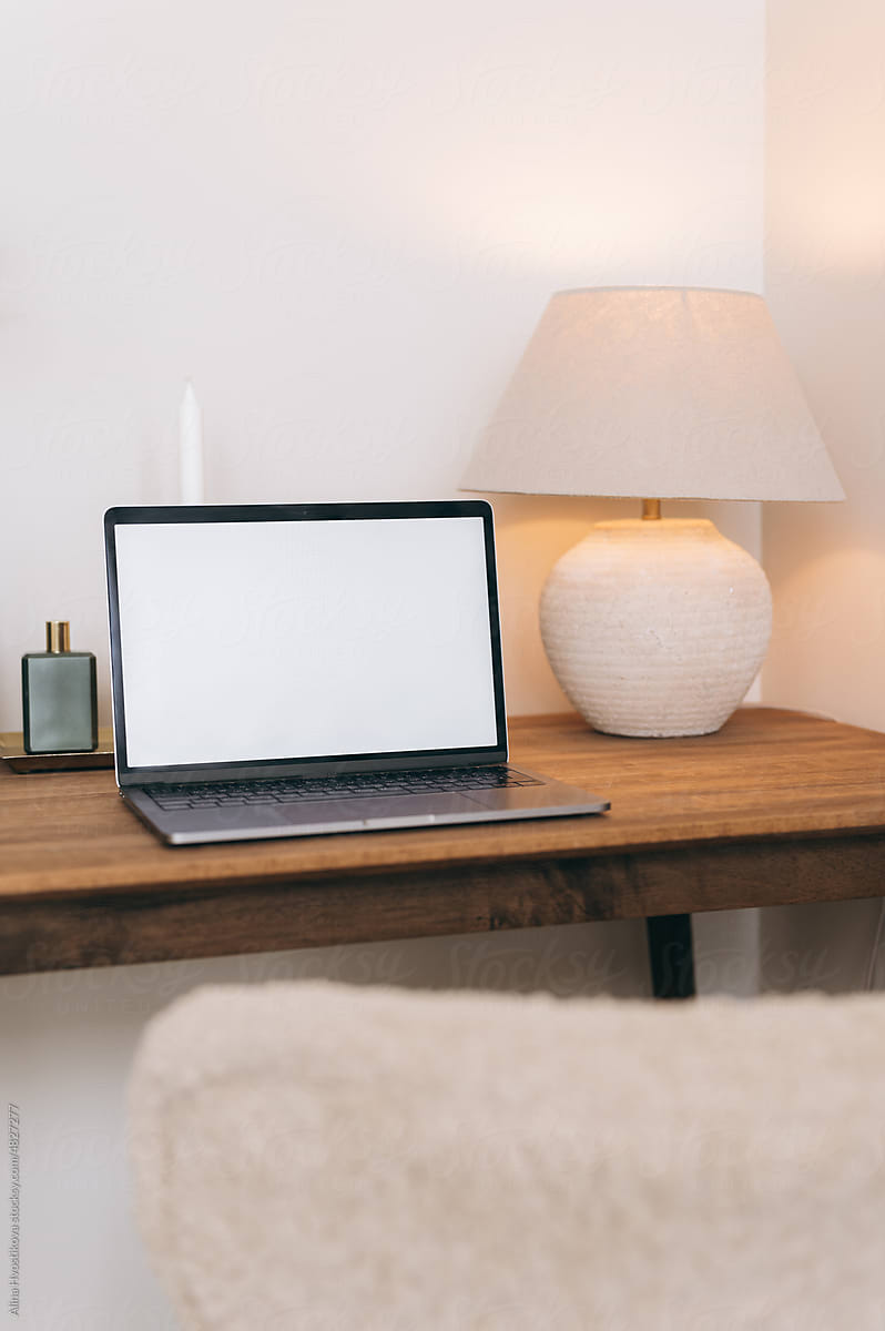 Laptop with blank screen on desk with vase and lamp