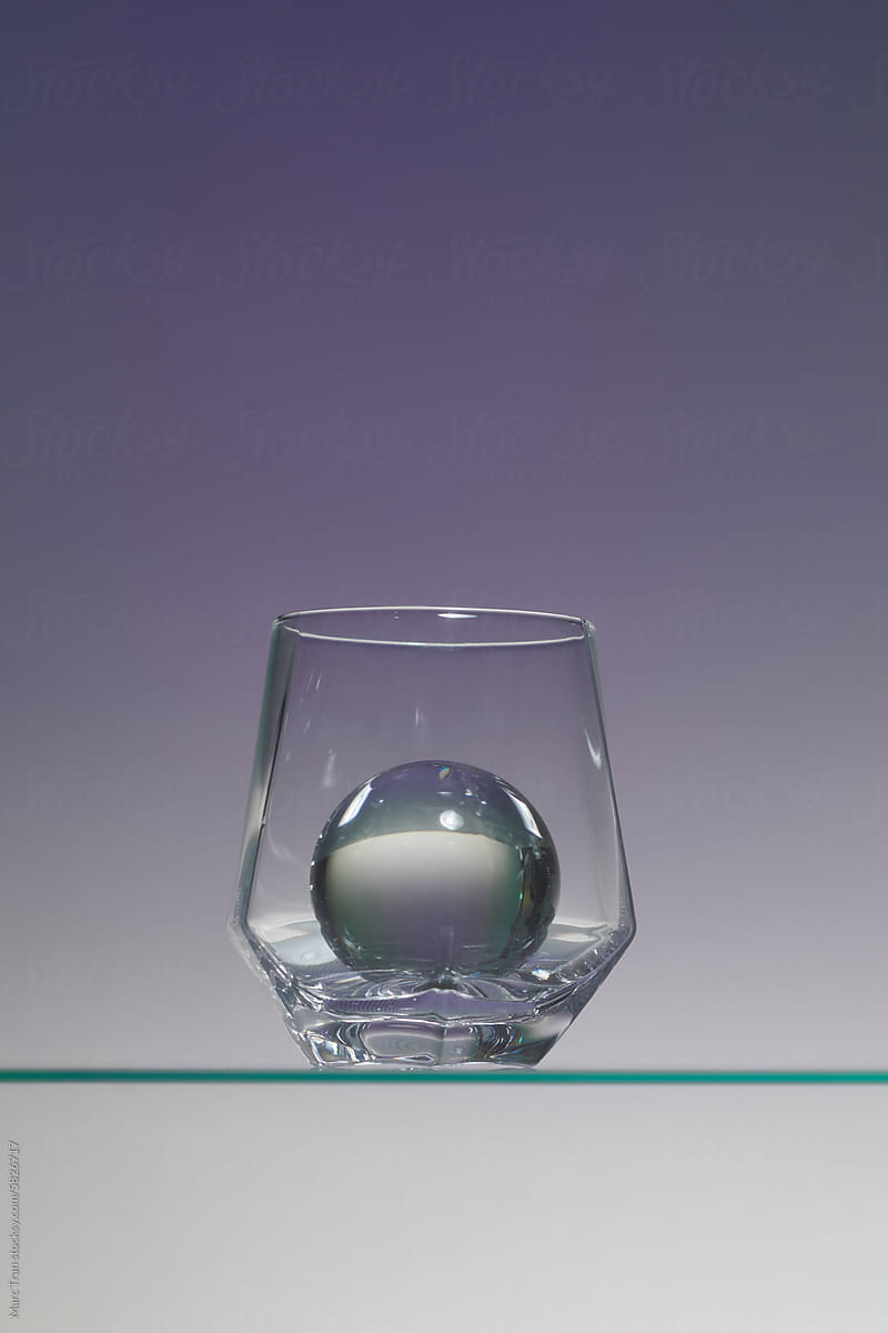 ice ball inside cocktail glass on a glass shelf over color background