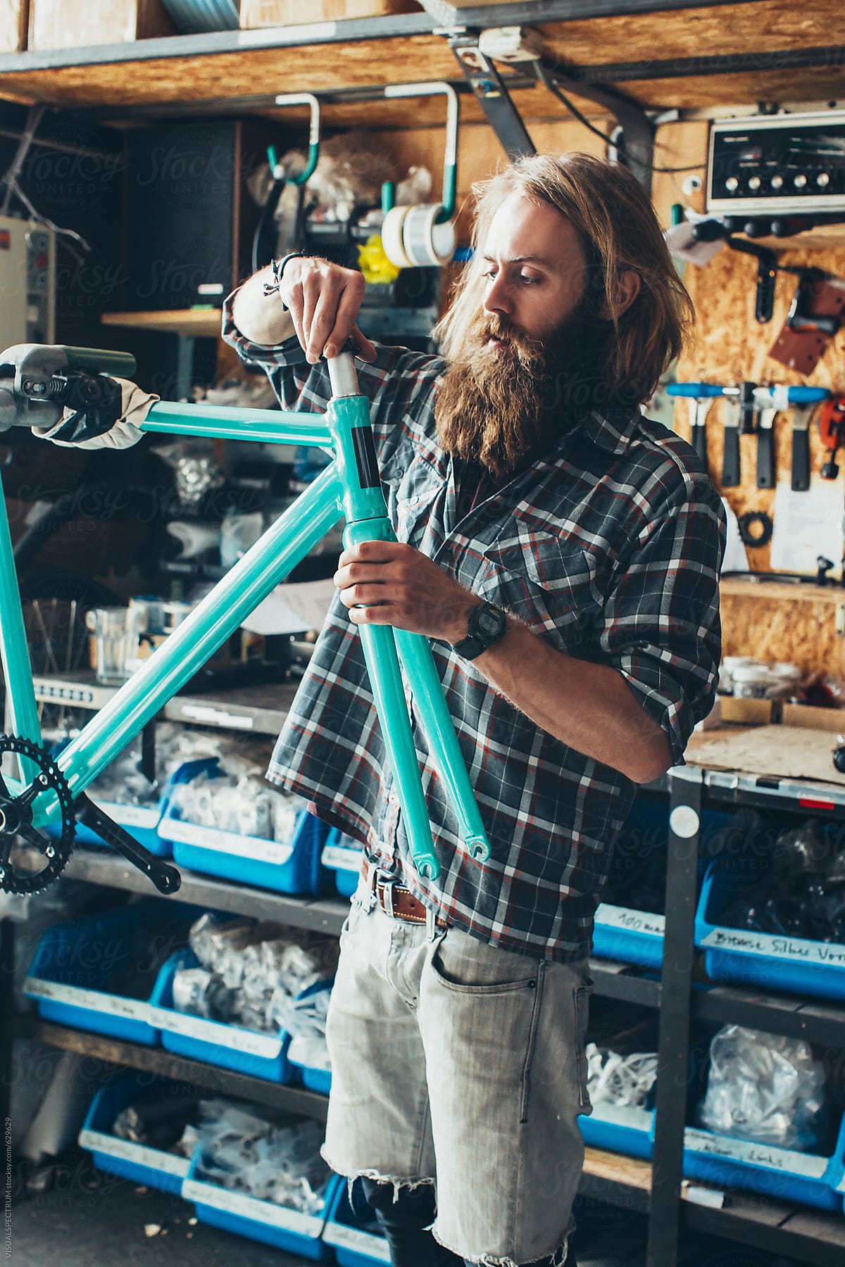 Long-Haired Hipster Mechanic Assembling Fixed Gear Bike in Bright Workshop