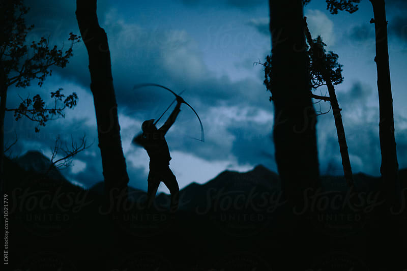 one adult male shoots bow and arrow at dusk in the forest