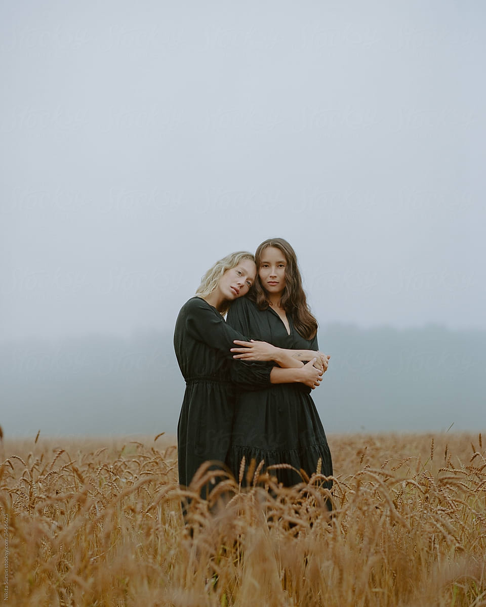 two girls in a black dress posing in a field among wheat ears